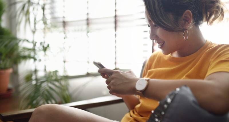 A woman sitting comfortably on a couch, focused on her phone, with a relaxed expression on her face.